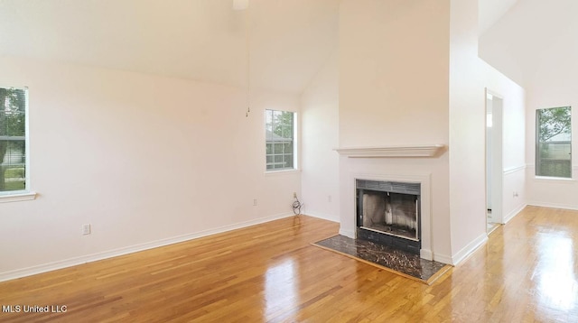 unfurnished living room with baseboards, a fireplace, high vaulted ceiling, and wood finished floors