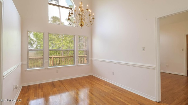 spare room featuring light wood-type flooring, a notable chandelier, and baseboards