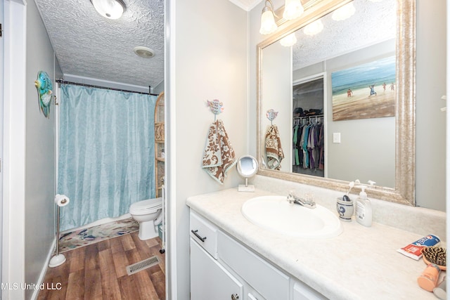 bathroom with wood finished floors, visible vents, toilet, vanity, and a textured ceiling