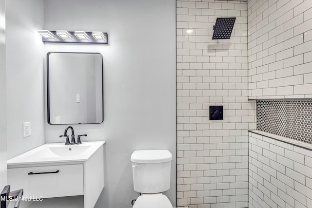 bathroom featuring a tile shower, vanity, and toilet