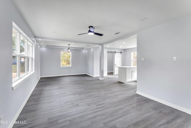 unfurnished living room featuring dark hardwood / wood-style flooring, a barn door, and ceiling fan