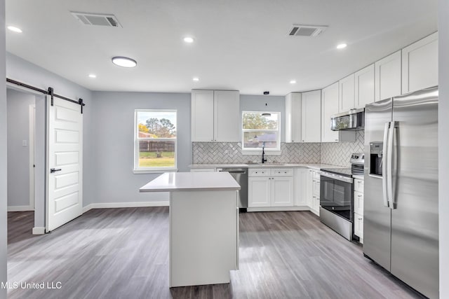 kitchen with white cabinets, a barn door, a healthy amount of sunlight, and appliances with stainless steel finishes