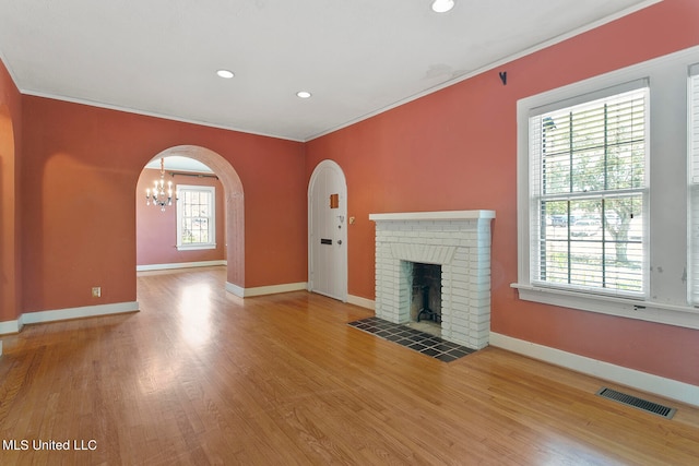 unfurnished living room with a notable chandelier, ornamental molding, a brick fireplace, and hardwood / wood-style floors