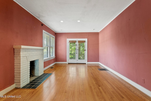 unfurnished living room featuring french doors, wood-type flooring, ornamental molding, and a brick fireplace