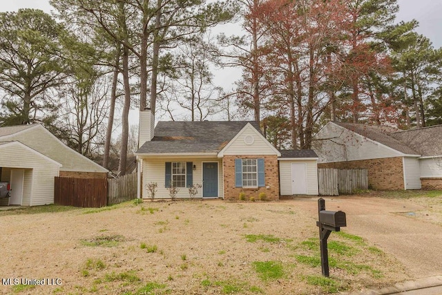 view of front facade featuring brick siding, a chimney, and fence