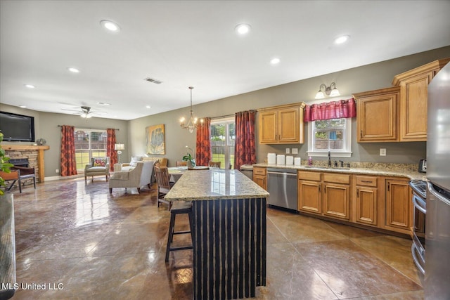 kitchen featuring sink, ceiling fan with notable chandelier, a kitchen island, stainless steel appliances, and pendant lighting