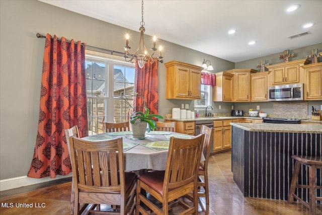 kitchen featuring light stone counters, stainless steel appliances, light brown cabinetry, and hanging light fixtures