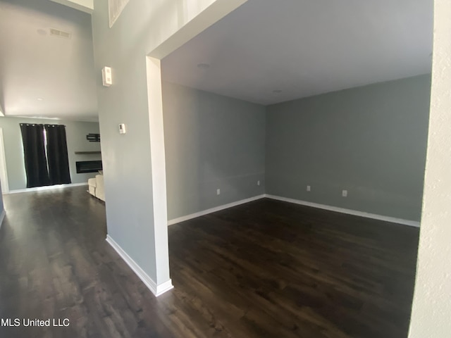 empty room featuring dark wood-style floors, a fireplace, and baseboards