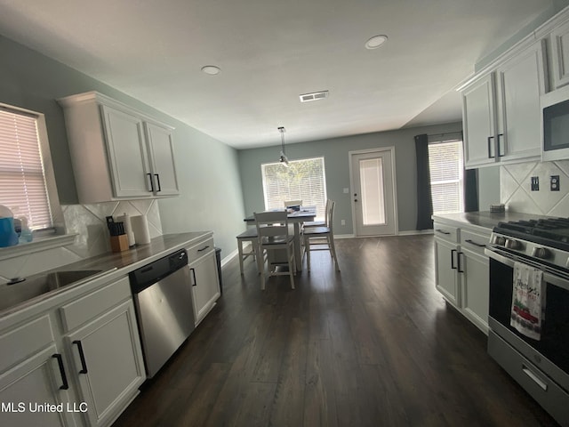 kitchen with dark wood-style floors, hanging light fixtures, decorative backsplash, appliances with stainless steel finishes, and baseboards