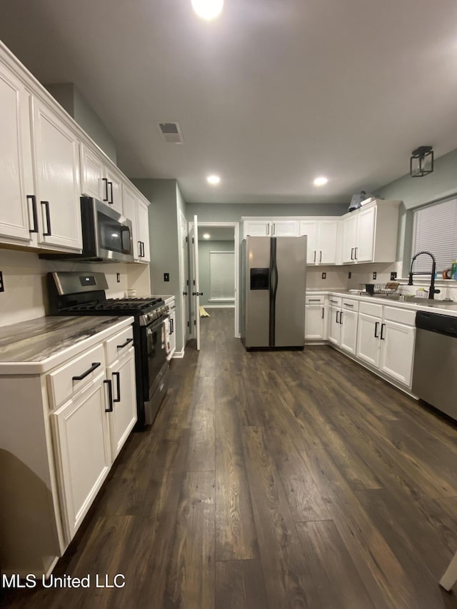 kitchen featuring dark wood-style flooring, visible vents, appliances with stainless steel finishes, white cabinetry, and a sink