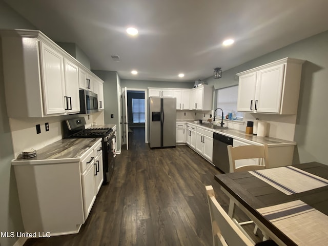 kitchen featuring recessed lighting, stainless steel appliances, a sink, white cabinets, and dark wood finished floors