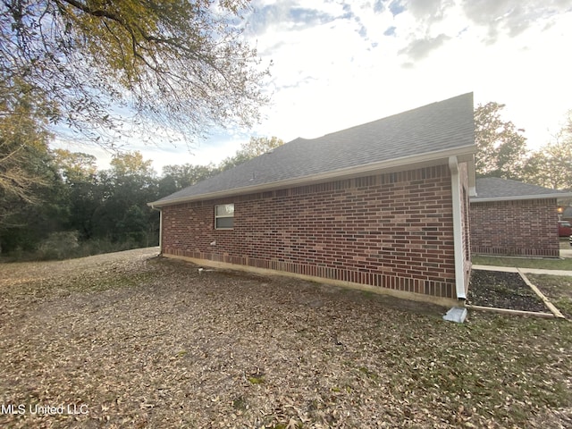 view of side of property with roof with shingles and brick siding