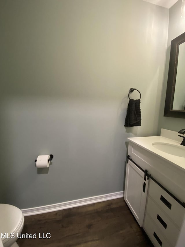 half bath featuring toilet, vanity, baseboards, and wood finished floors