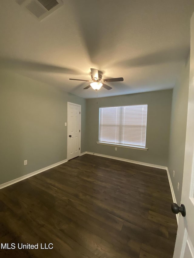 empty room featuring ceiling fan, dark wood finished floors, visible vents, and baseboards