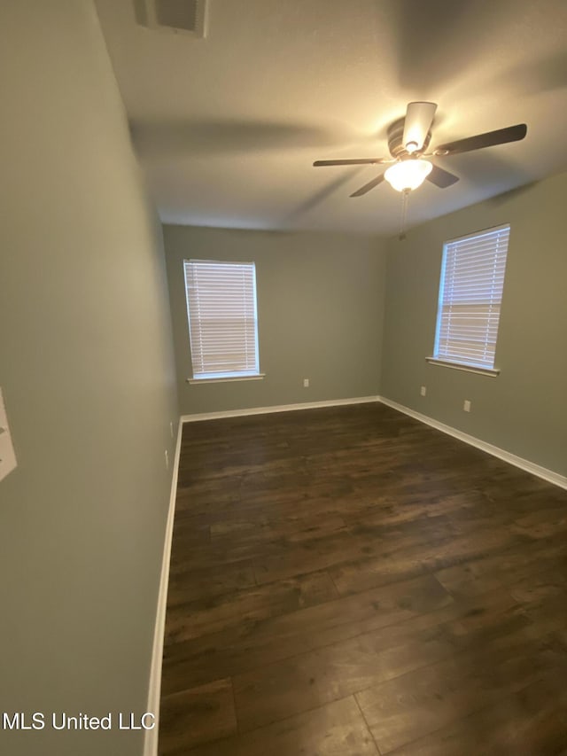 empty room with ceiling fan, visible vents, baseboards, and dark wood finished floors