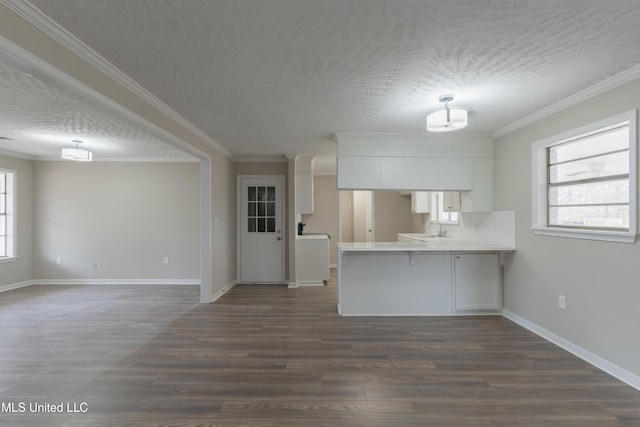 kitchen with dark wood-type flooring, a sink, plenty of natural light, white cabinetry, and a peninsula