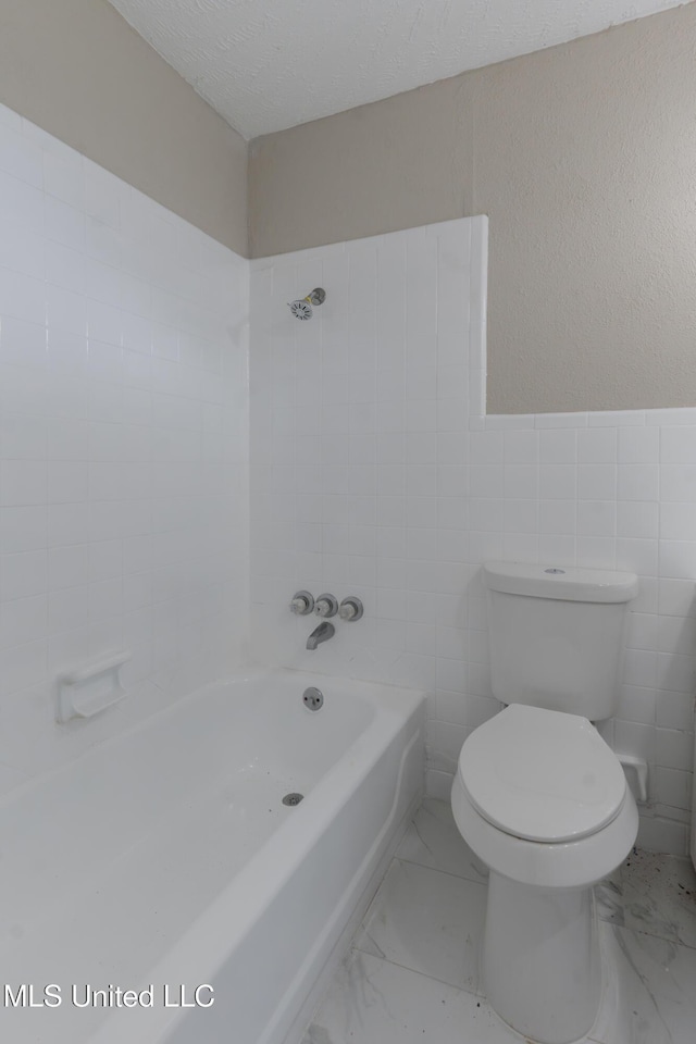 full bath with shower / bath combination, a textured ceiling, tile walls, toilet, and marble finish floor