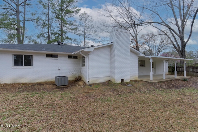 view of side of home featuring a lawn, central AC, fence, brick siding, and a patio area