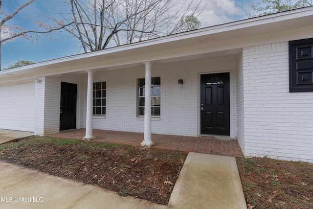 entrance to property with brick siding, covered porch, and a garage