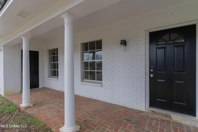 doorway to property with brick siding, visible vents, and covered porch