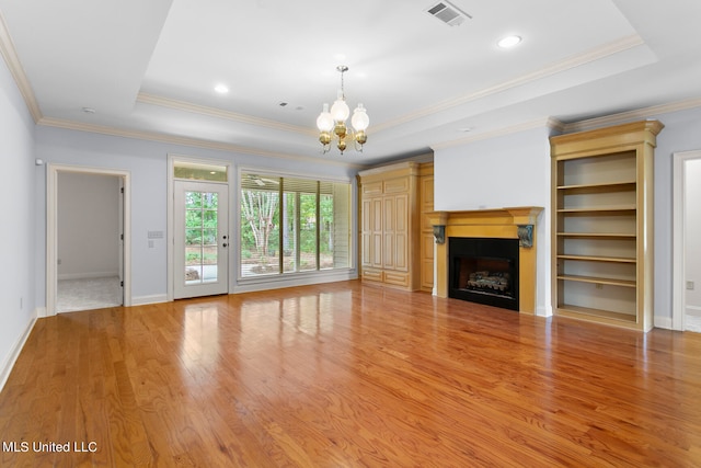 unfurnished living room featuring light hardwood / wood-style floors, a notable chandelier, a tray ceiling, and crown molding