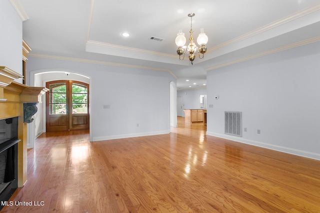 unfurnished living room with french doors, a tray ceiling, crown molding, a notable chandelier, and light hardwood / wood-style floors