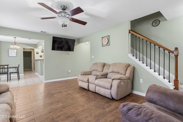 living room featuring ceiling fan with notable chandelier, a textured ceiling, and wood-type flooring