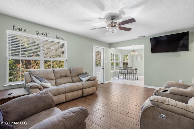 living room with ceiling fan with notable chandelier and a textured ceiling