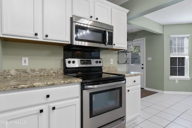 kitchen with light stone counters, a textured ceiling, light tile patterned floors, white cabinetry, and appliances with stainless steel finishes