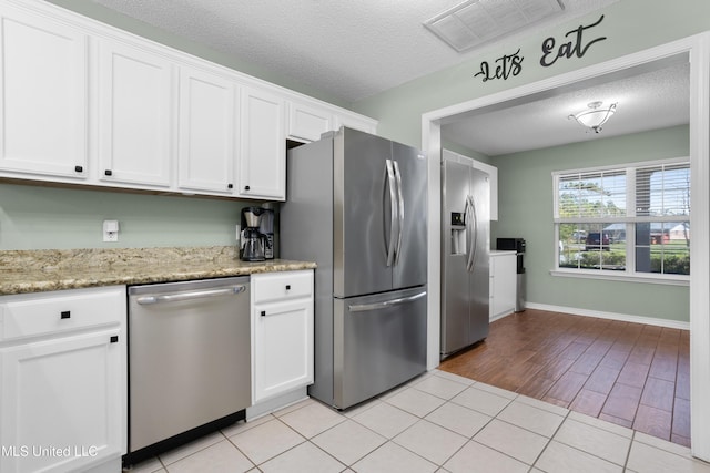 kitchen featuring light stone counters, stainless steel appliances, a textured ceiling, and white cabinets