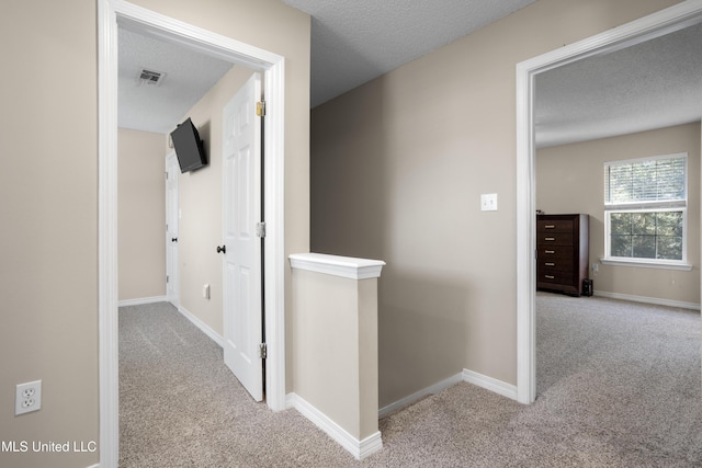 corridor with a textured ceiling and light carpet