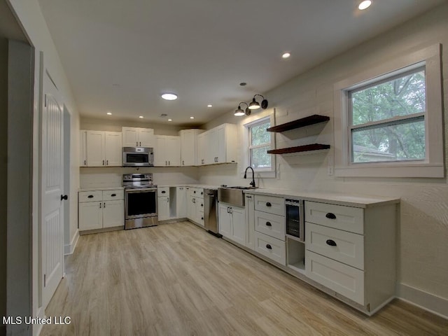 kitchen with appliances with stainless steel finishes, a sink, light wood-style flooring, white cabinetry, and baseboards