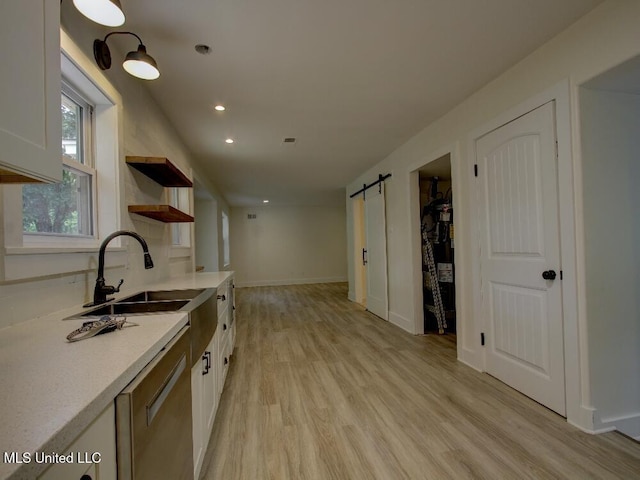 kitchen featuring a sink, light wood-style floors, a barn door, light countertops, and white cabinetry