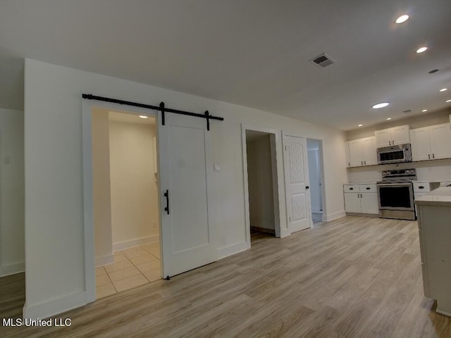 kitchen featuring stainless steel appliances, a barn door, light countertops, white cabinetry, and light wood-type flooring
