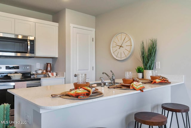 kitchen featuring a kitchen breakfast bar, kitchen peninsula, sink, white cabinetry, and appliances with stainless steel finishes