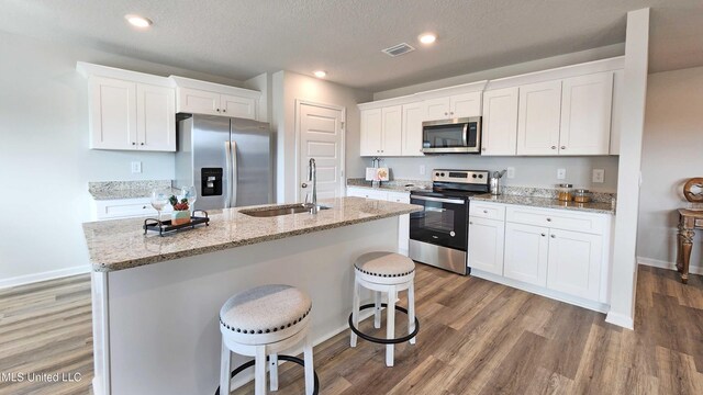 kitchen with visible vents, wood finished floors, an island with sink, a sink, and appliances with stainless steel finishes