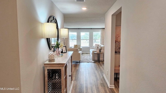 corridor featuring baseboards, visible vents, a textured wall, and wood finished floors