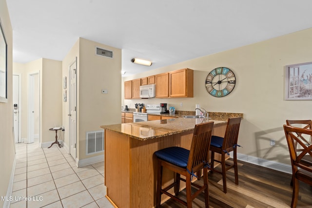 kitchen featuring white appliances, sink, light wood-type flooring, stone countertops, and kitchen peninsula