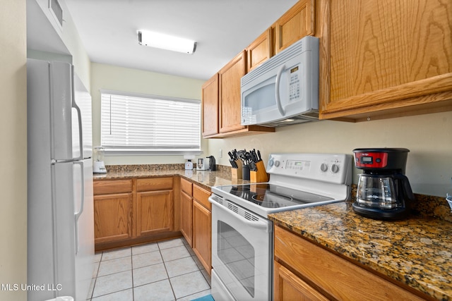 kitchen featuring light tile patterned floors, white appliances, and dark stone countertops