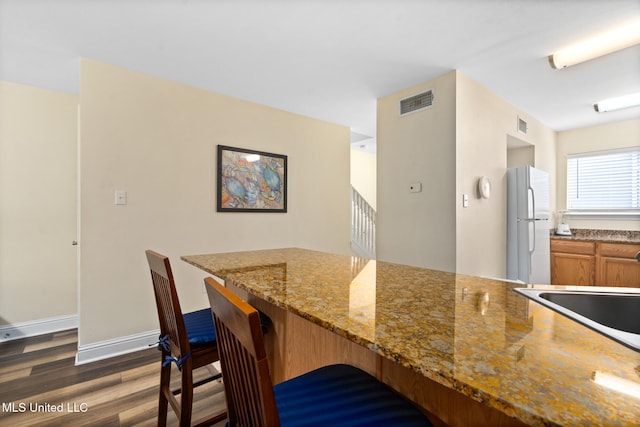 kitchen with dark hardwood / wood-style floors, white refrigerator, and light stone countertops