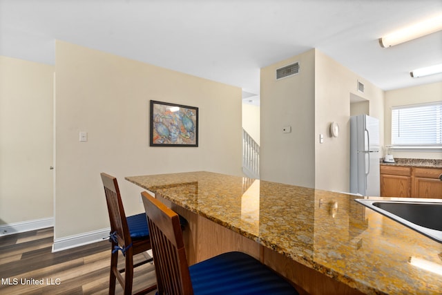 1664 Beach Blvd Unit 90, Biloxi, MS 39531 - kitchen with freestanding refrigerator, dark wood finished floors, a breakfast bar area, light stone countertops, and brown cabinets