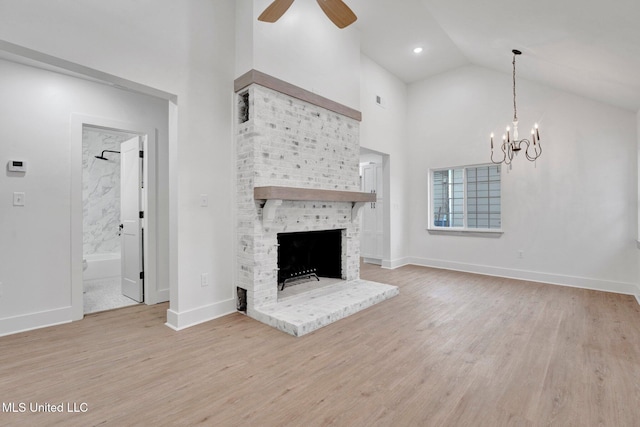 unfurnished living room with high vaulted ceiling, ceiling fan with notable chandelier, wood finished floors, a fireplace, and baseboards