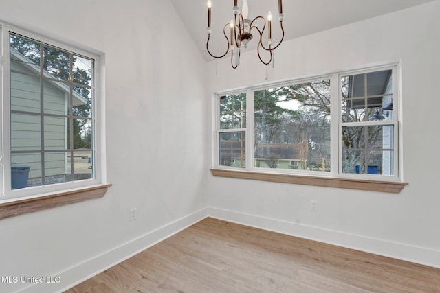 empty room with a notable chandelier, lofted ceiling, baseboards, and wood finished floors