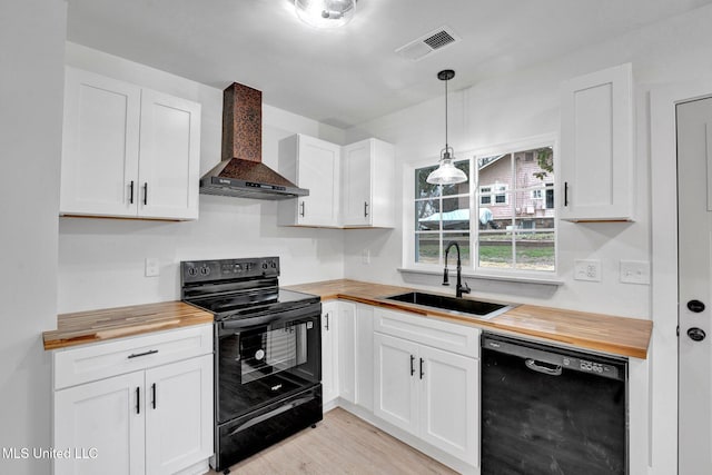 kitchen featuring visible vents, black appliances, a sink, butcher block counters, and wall chimney range hood