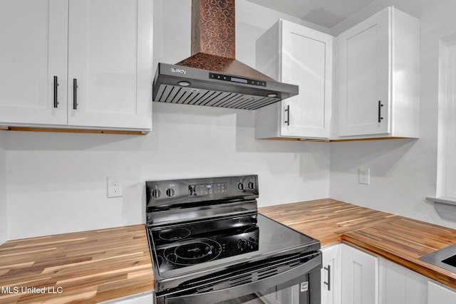 kitchen featuring wall chimney range hood, black / electric stove, white cabinets, and wood counters