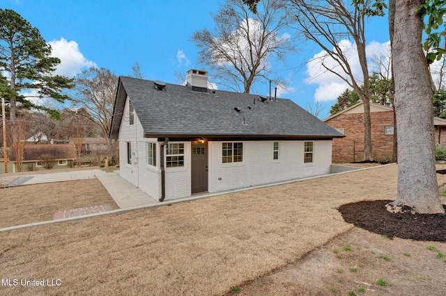 rear view of house featuring brick siding, roof with shingles, a lawn, a chimney, and a patio