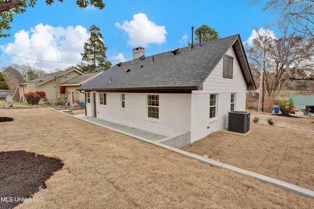 back of house with a patio, cooling unit, a chimney, a shingled roof, and brick siding