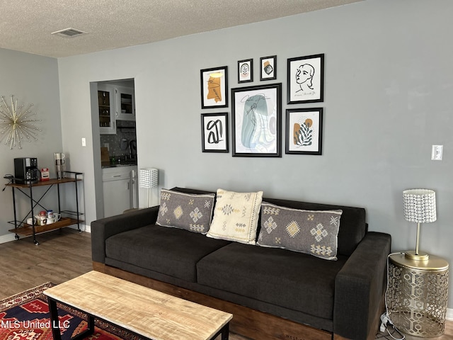 living area featuring dark wood-style flooring, visible vents, a textured ceiling, and baseboards