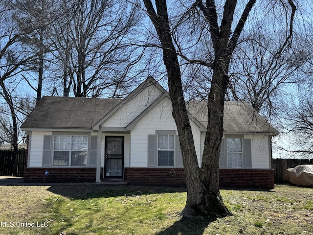 view of front facade featuring a shingled roof, a front yard, fence, and brick siding