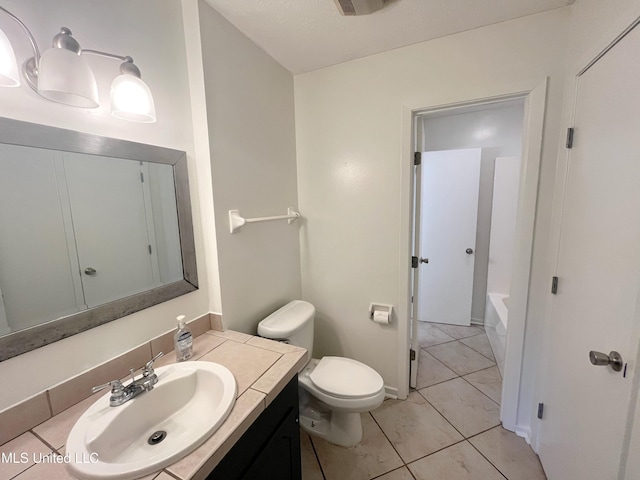 bathroom with tile patterned floors, a washtub, vanity, and toilet